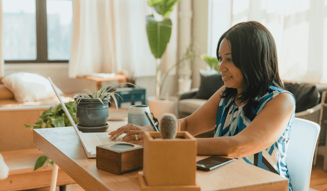 Woman working at a laptop in a cozy home office, showcasing a clear video call setup with plants and a tidy workspace.