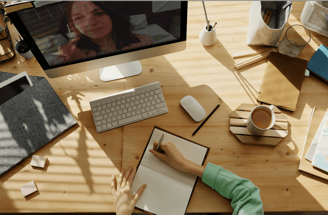 A person takes notes while participating in a virtual meeting on a computer, emphasizing the importance of eye contact.