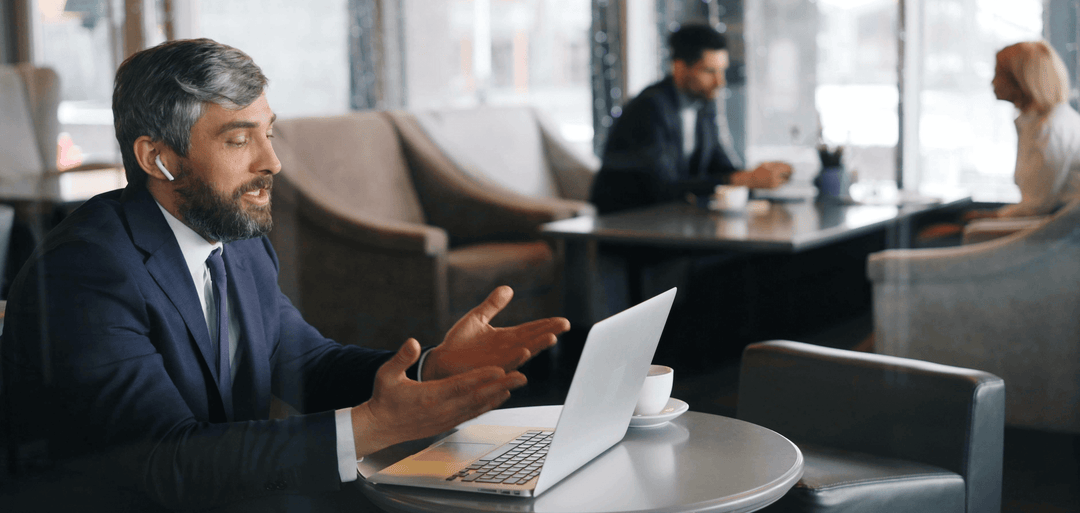 Professional man in a suit engaged in a video call at a cafe, showcasing clear communication and technology use.